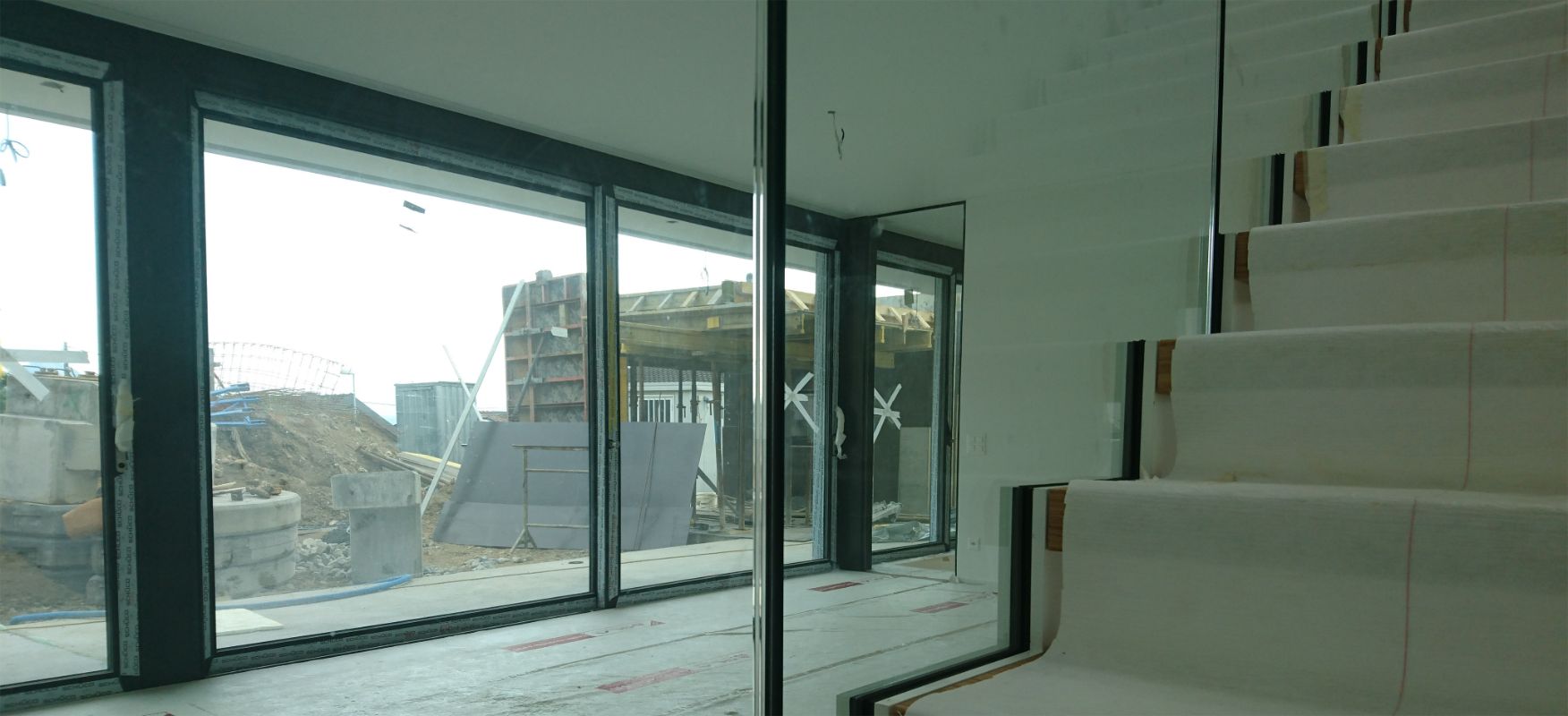 Chantier de construction, grande fenêtre et escalier intérieur.